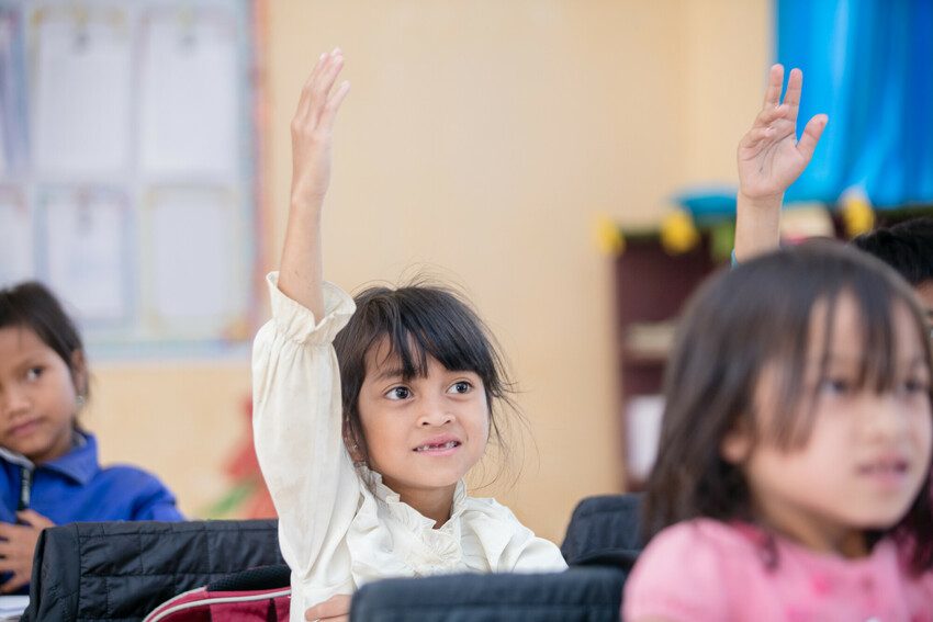 Girl raises her hand to ask a question in a classroom in Kon Tum Province, Vietnam.