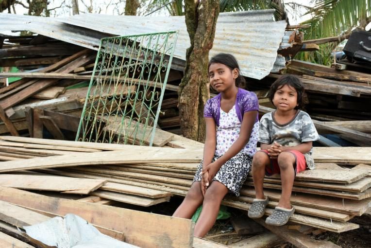 Children sit on piles of wooden timber from destroyed houses