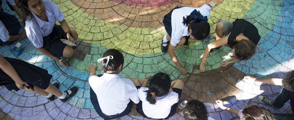 Children in Thailand chalk a rainbow on the ground.