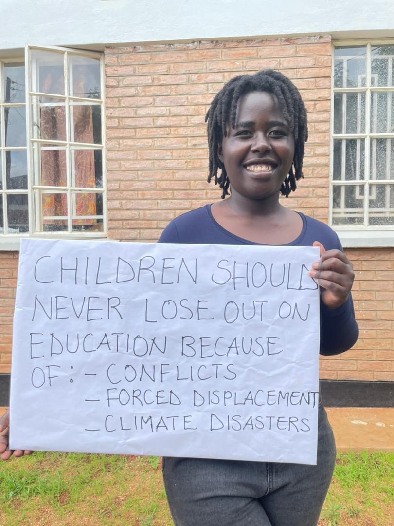 Angela from the Y4EiE panel holding a sign: ‘children should never lose out on education because of: conflicts, forced displacement, climate disasters ’
