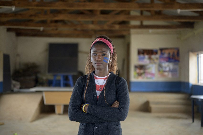Gradi, an activist from Mali stands in a classroom with Girls Get Equal stripes on her face in blue.