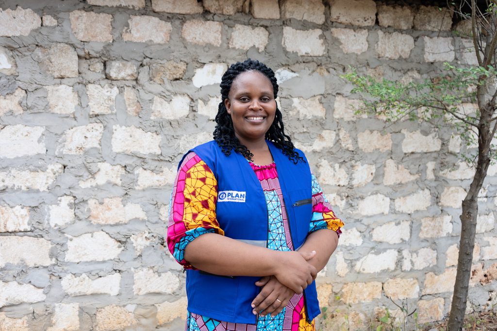 Programme Unit Manager Winifred stands by the school, smiling, arms crossed.