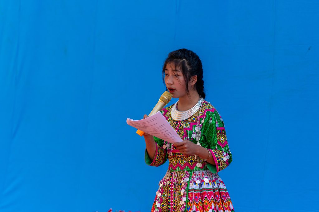 Dung standing, holding a microphone and reading from her note paper.