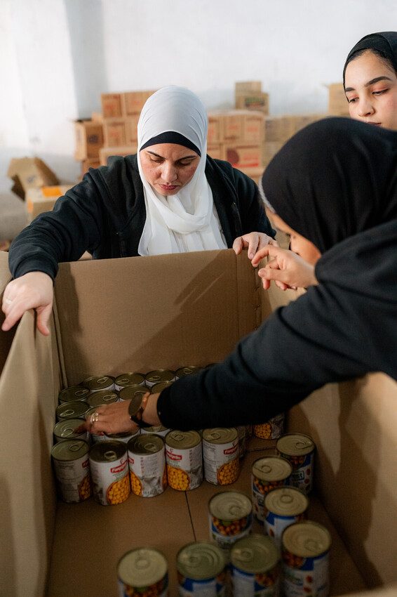 Plan staff loading a box filled with canned food for Gaza. 