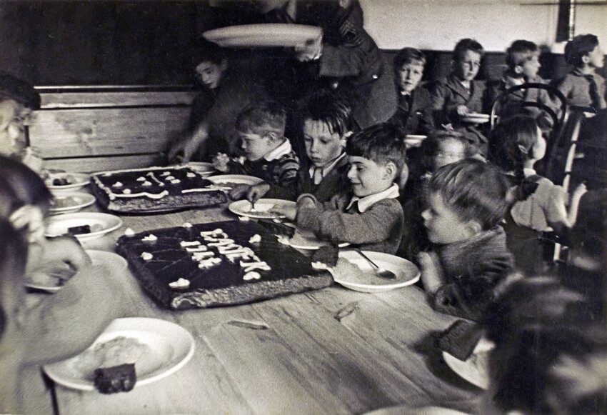 Children at a table, the focus is on a boy eating cake. Black and white photo 1944. 
