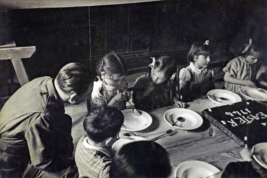 Young girls eat cake and speak to an army officer. Black and white photo 1944. 