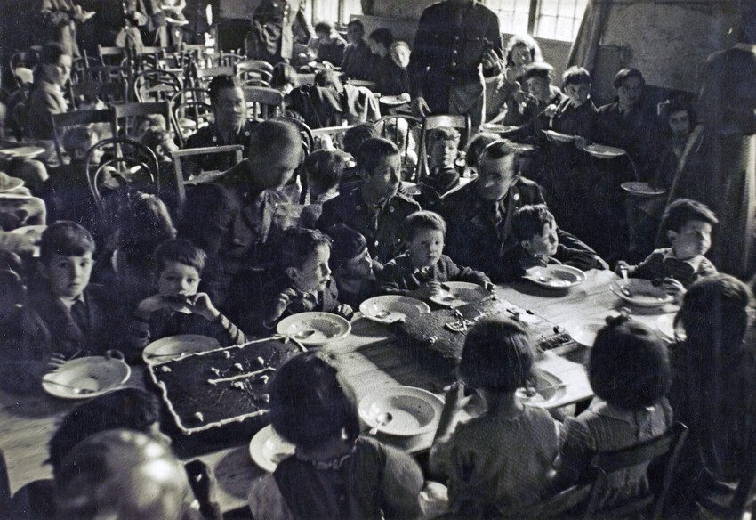 Children sit at a table enjoying the tea party. Black and white photo 1944. 
