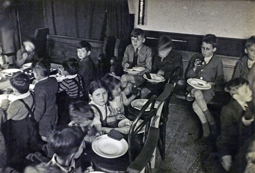 Children enjoying plates of cakes on their laps. Black and white photo 1944. 