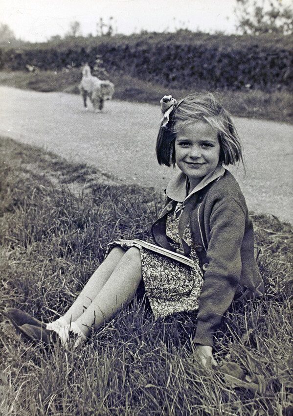 A young girl sitting on a grass verge.