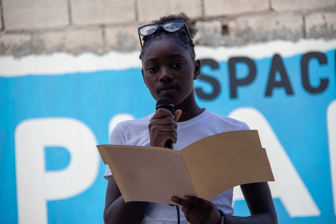 A girl reads from an open folder into a microphone. 