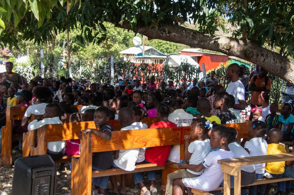 An audience of children sit on benches.
