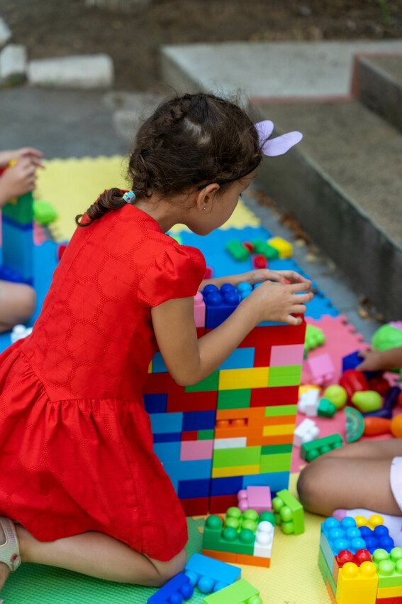 A girl plays with Lego, building a wall. 