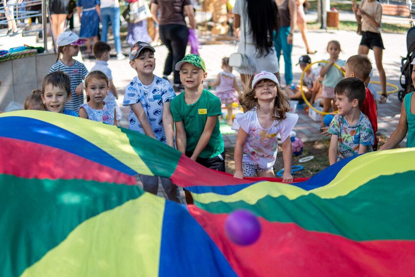 Children hold the edge of a toy parachute. 