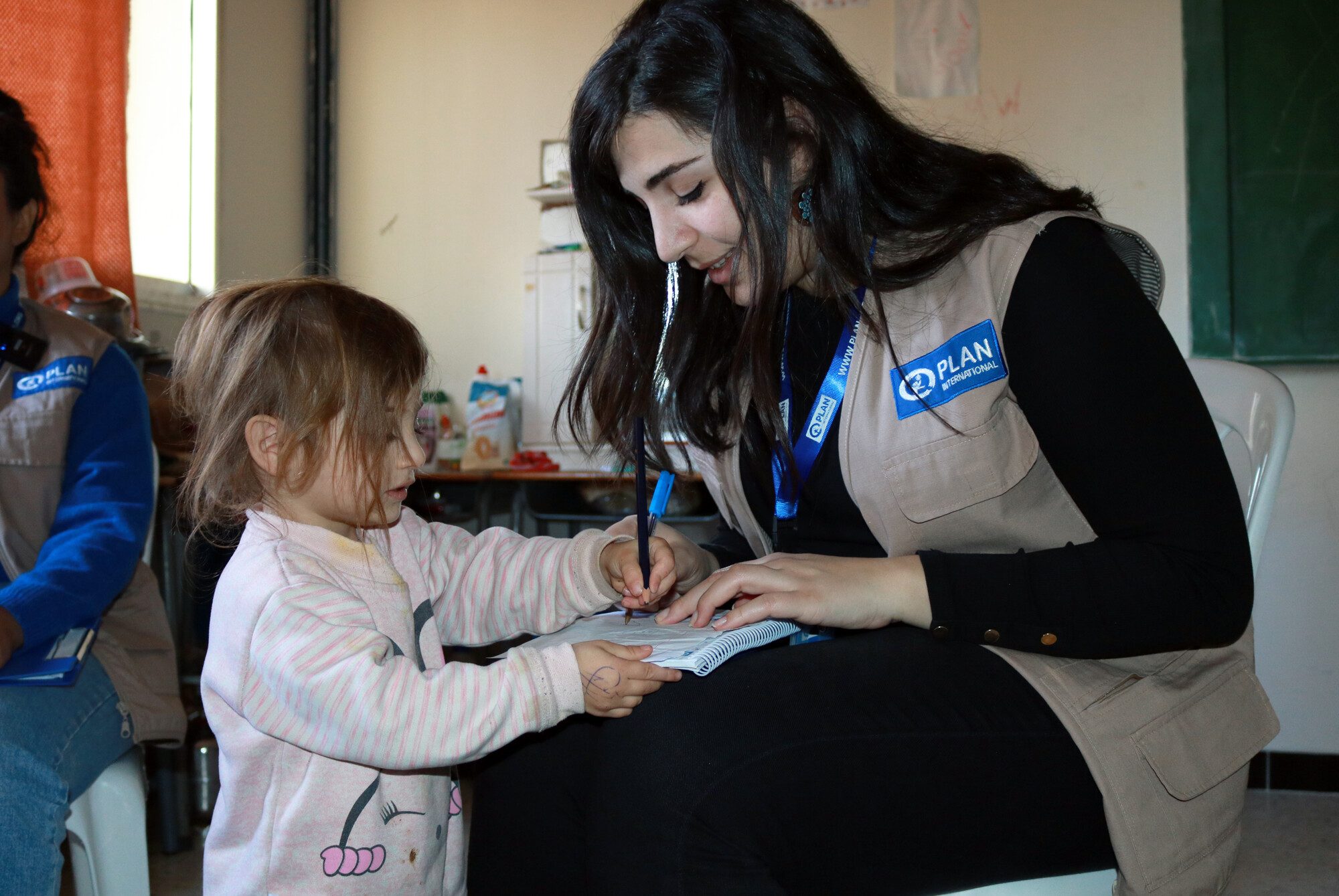 Aseel, 2, shows her drawing skills to Plan staff member.