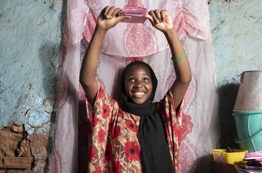 Faulat, 21, Kenya holds up a sanitary  pad, smiling. 