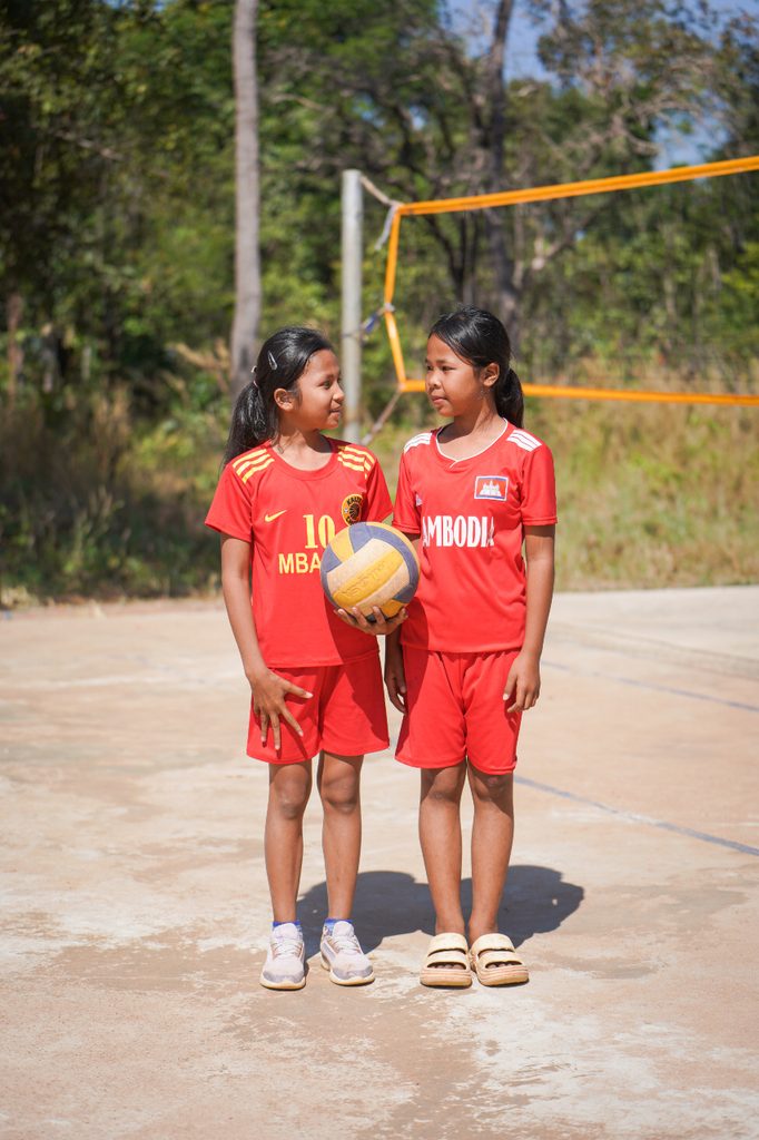 Girls in football kit hold football and smile at each other.