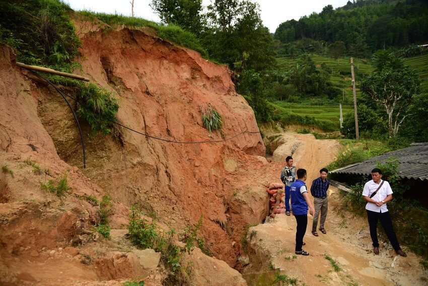 Plan staff and community members stand speaking next to a ravine and landslide. 