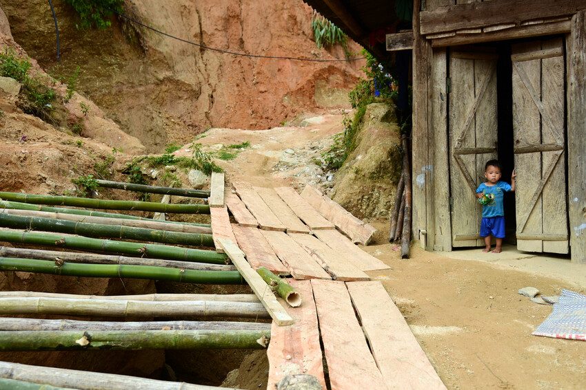A young child stands outside the front of a house which now sits very close to a large ravine. 