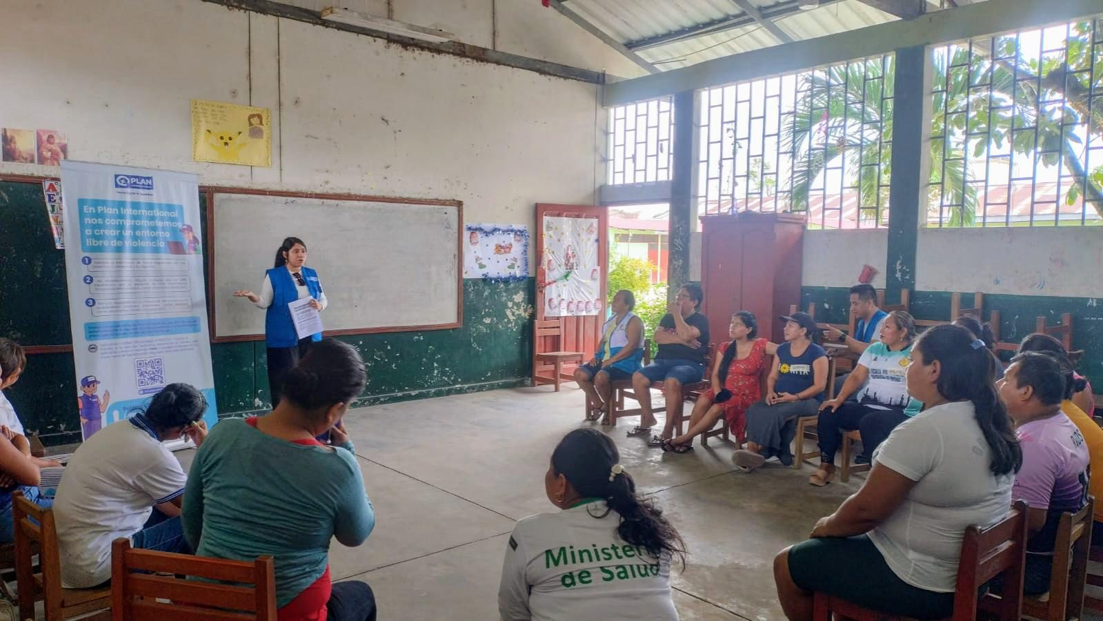 Roxana stands at the front of a room of people sitting on chairs talking.
