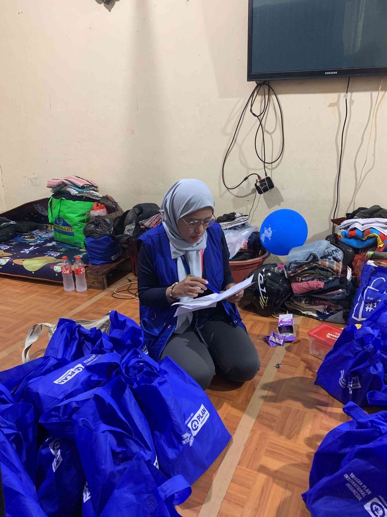 Maulinna is kneeling on the floor checking off bags against a sheet of paper.