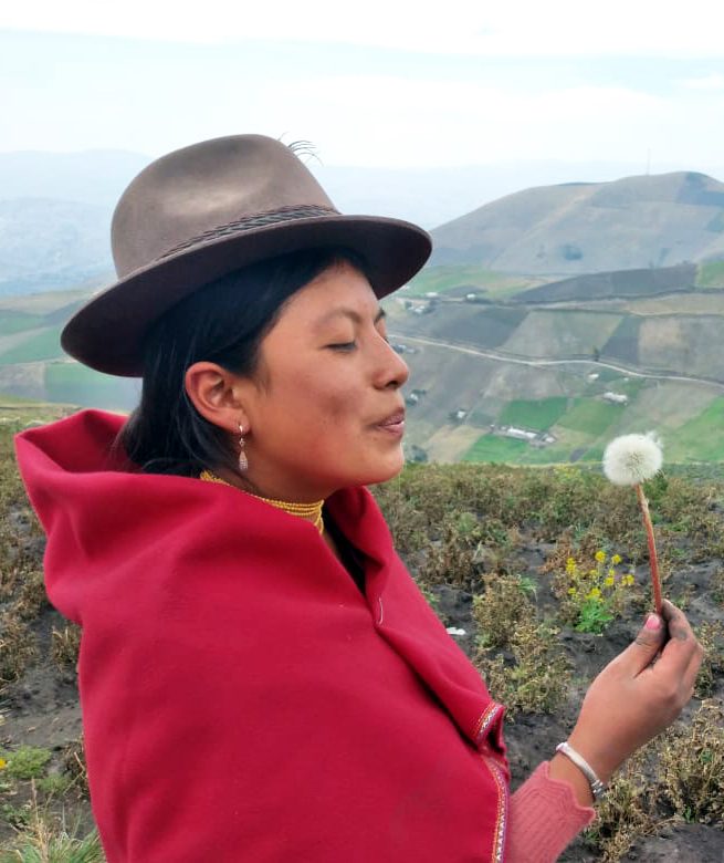 A young woman blows on a flower. 