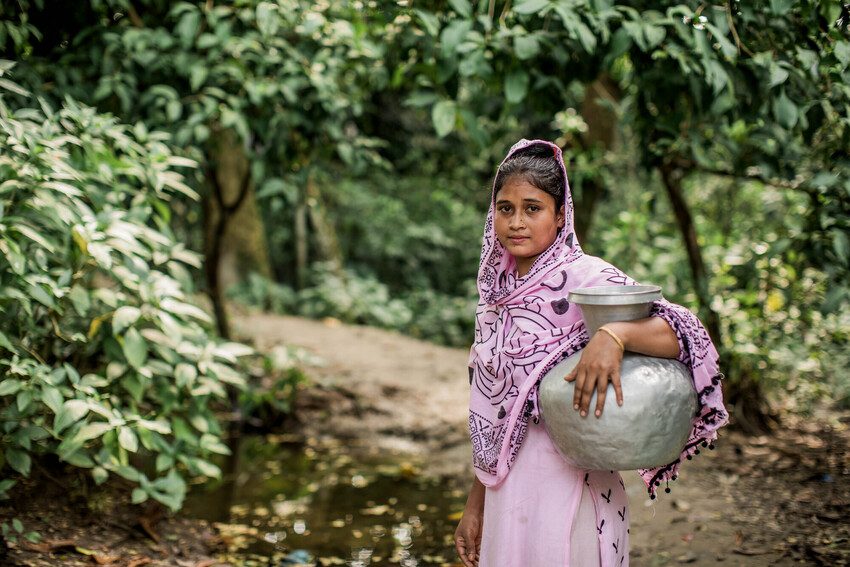 Girl standing holding a large metal pot. 