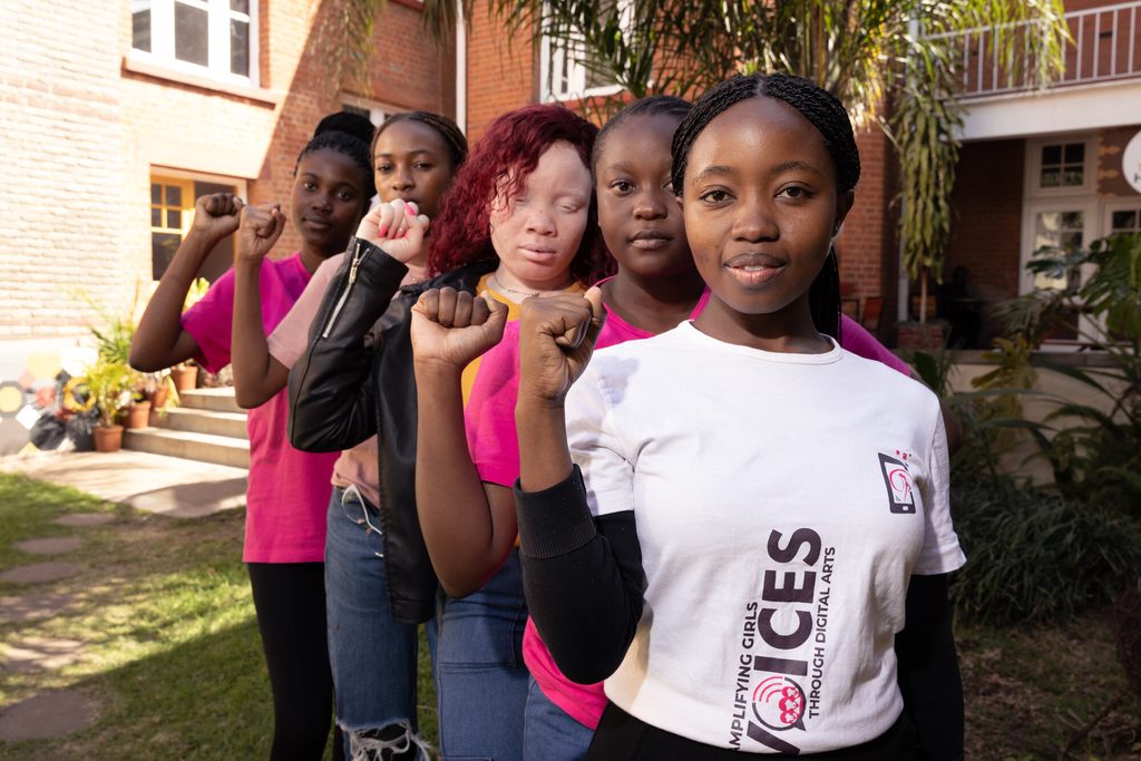 Girls in Zimbabwe lining up with raised fists to challenge harmful traditions like child marriage.