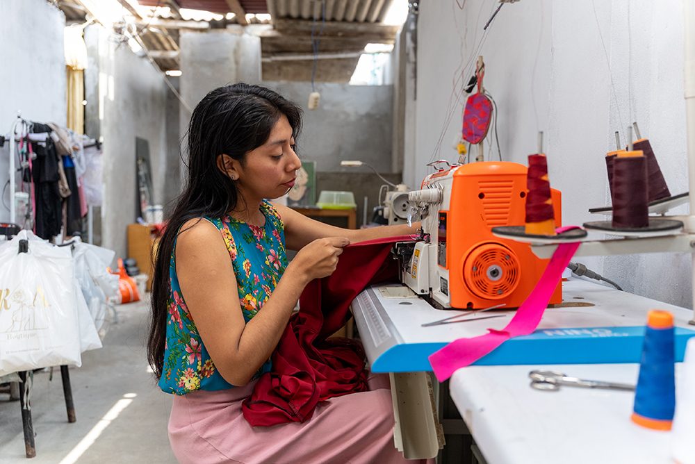 Rossi cosiendo un vestido en su taller. © Plan International