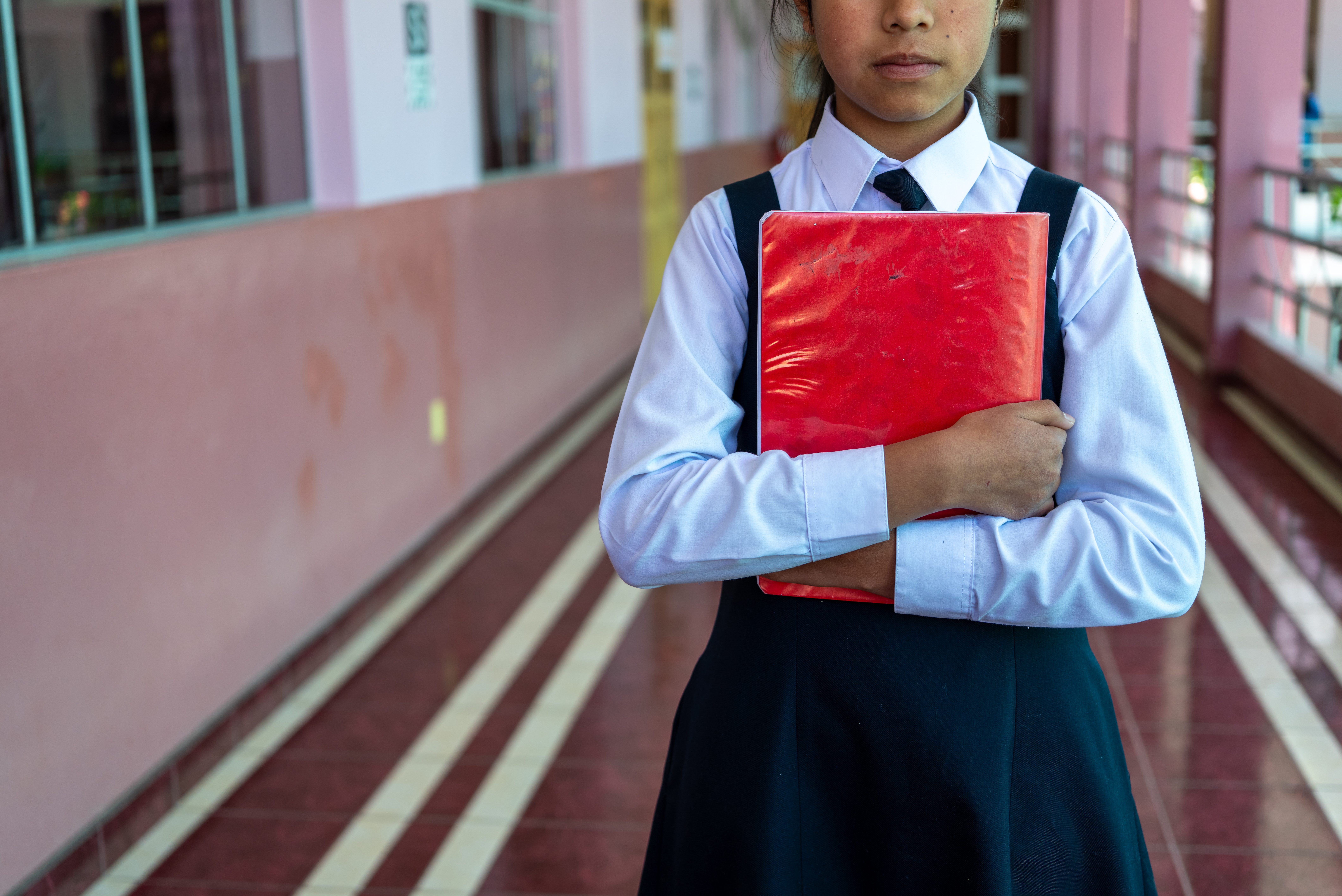 Adolescente con cuaderno en escuela con rostro cubierto, denotando problemáticas en aulas.