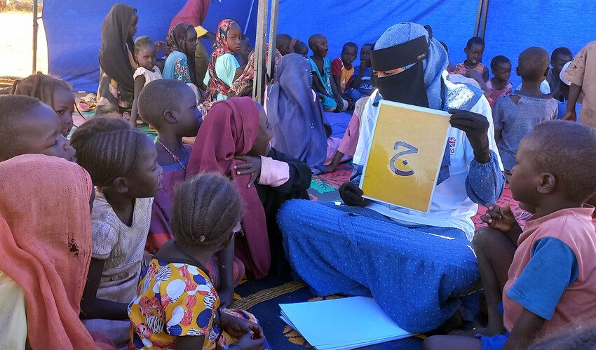 An educator holds up a letter and a group of young children sit around to learn it. 