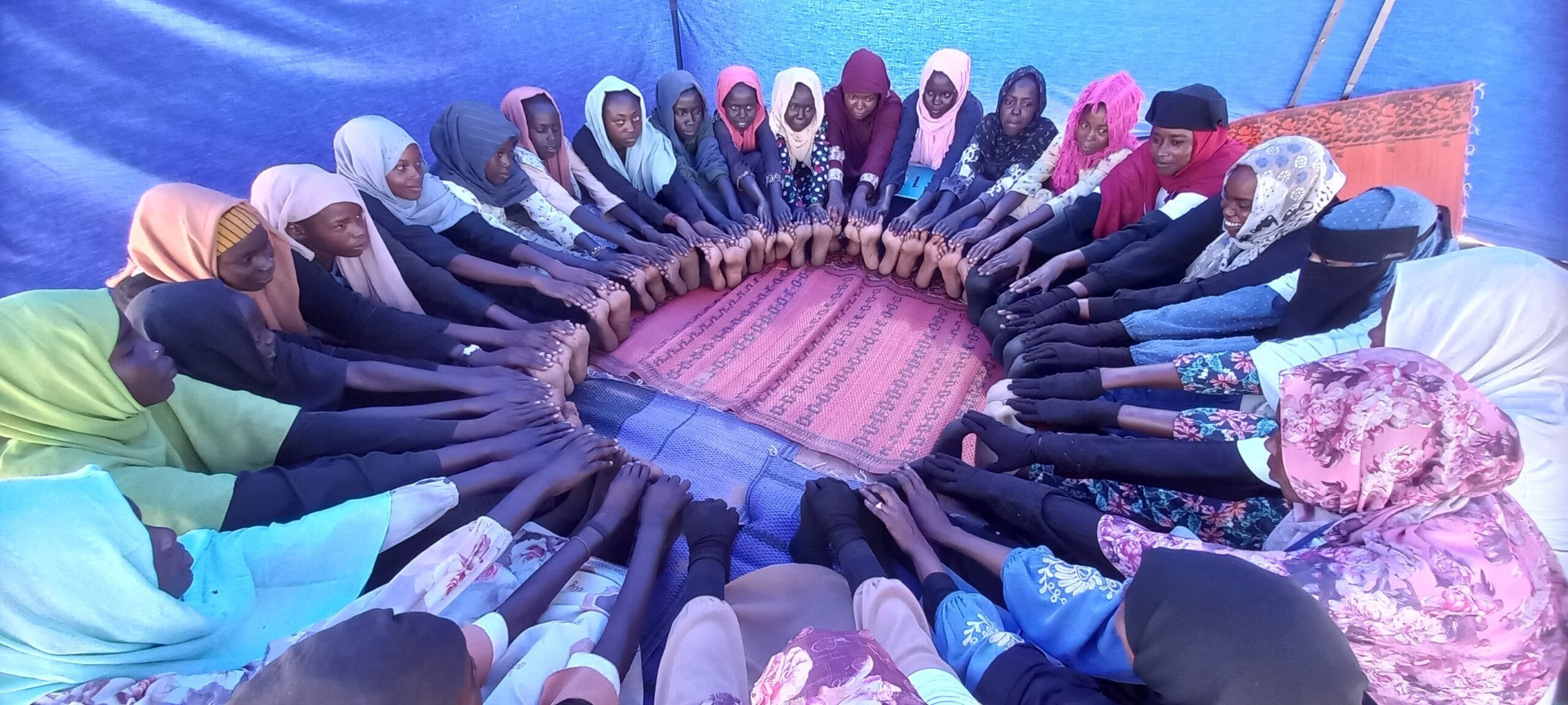 Girls sit in a circle and place together their feet and hands as part of the lotus exercise.