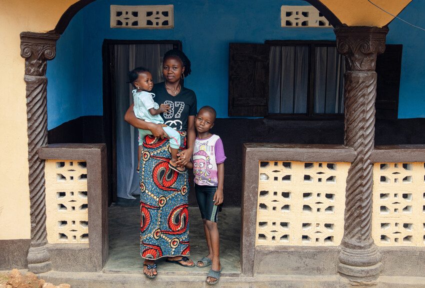Kumba stands with her 2 children. 