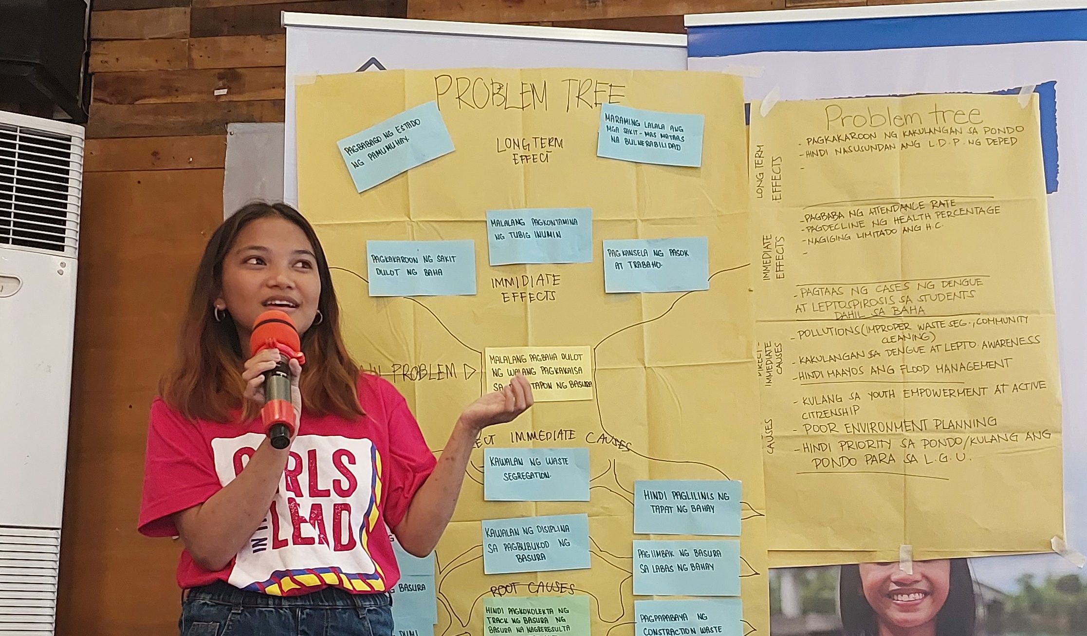 Aires stands in front of the board showing the problem tree and talks into a microphone.