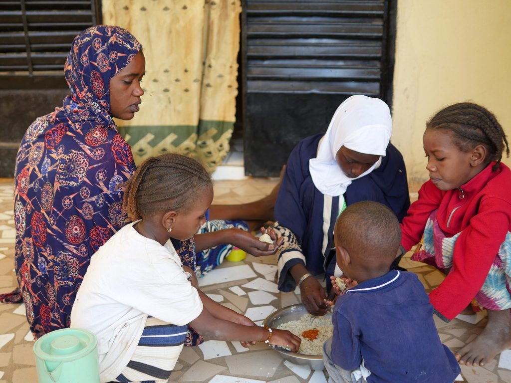 Aissata and her children sharing a meal in their yard.