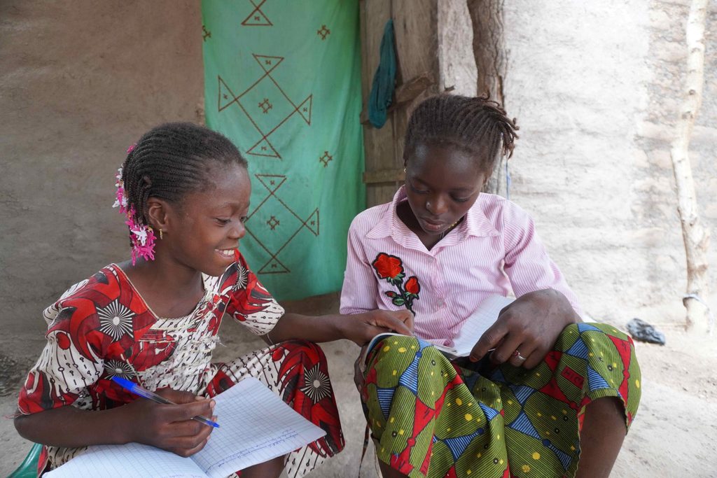 Diatou with her sister writing in their exercise books at home.