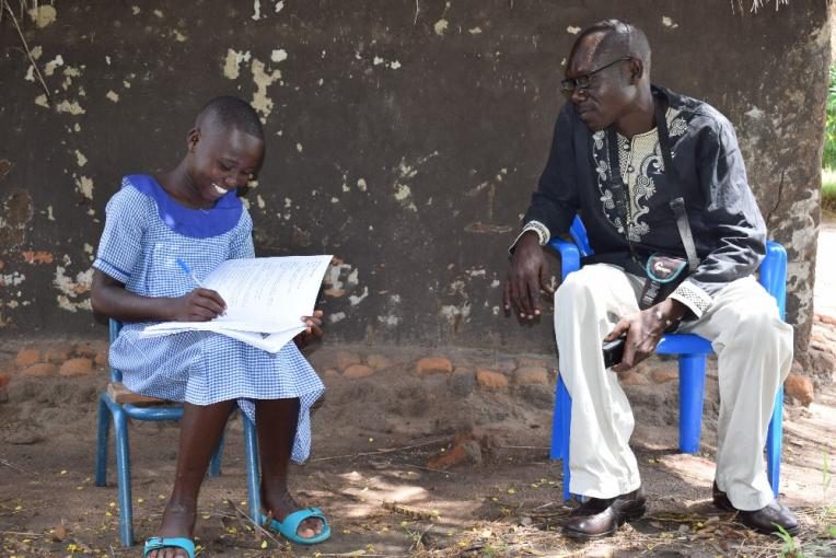 Bridget, 13, completing her homework with help from a teacher in Rhino refugee settlement