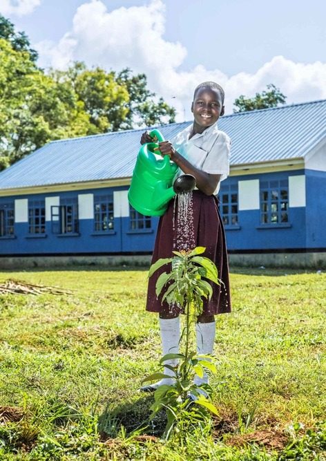 A girl uses a watering can to water a plant.