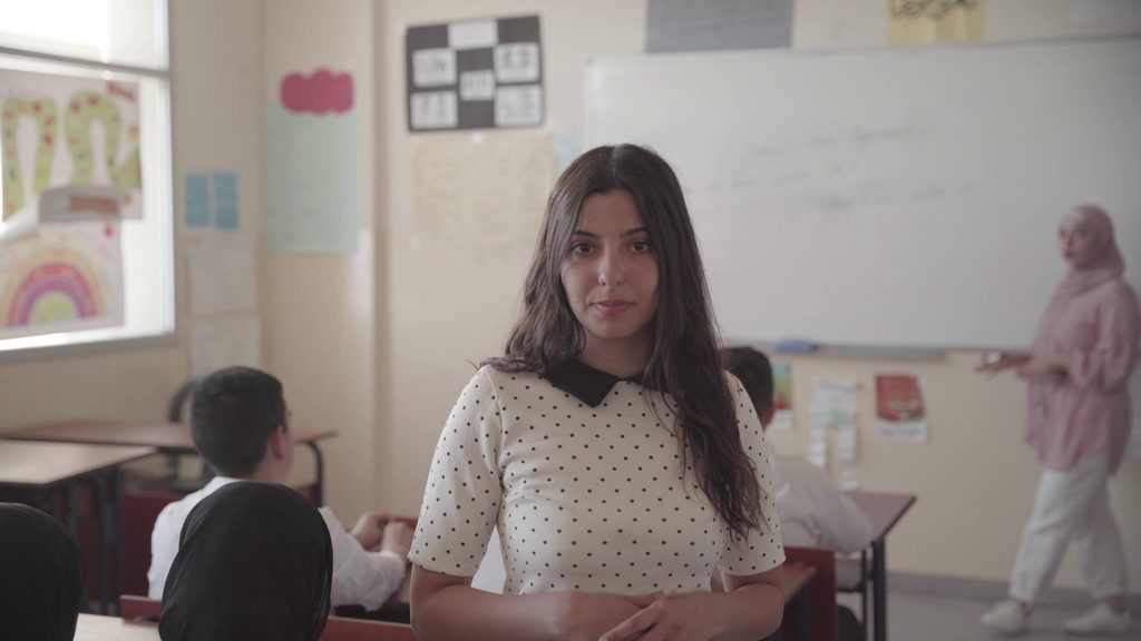 Young student standing in the middle of a classroom that looks almost empty in the background due to school dropouts among youth.