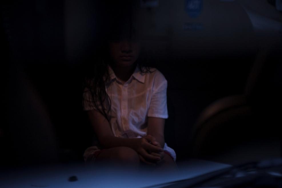 A girl sits, hidden in the shadows of a dark corner