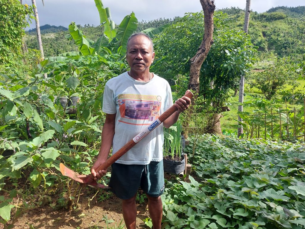 Roberto holding a pick mattock included in the distributed gardening tools 