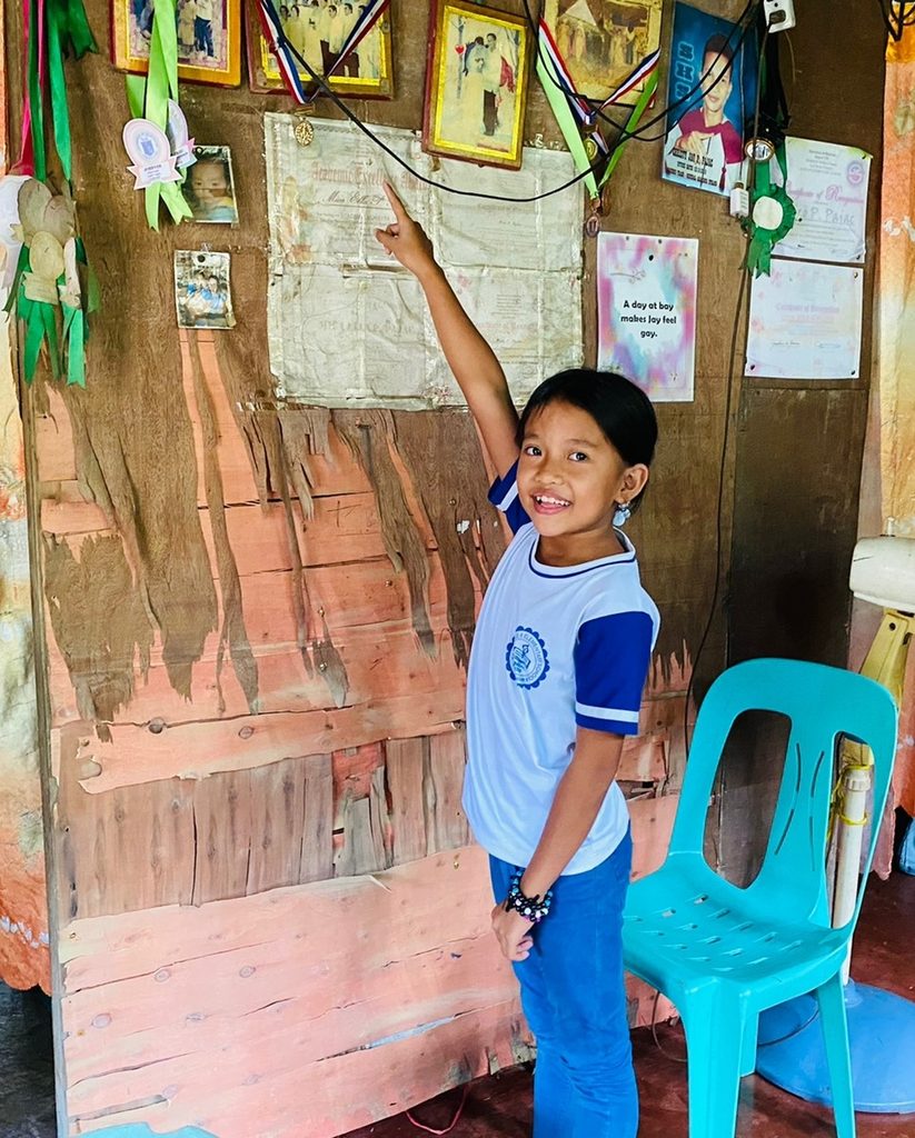 Girl points to a wall decorated with school awards