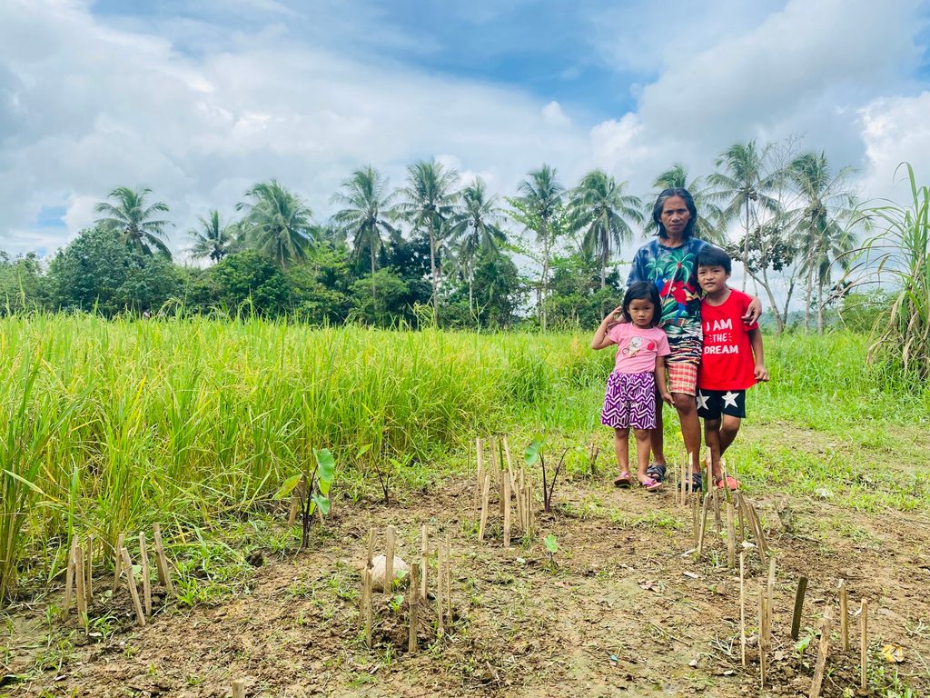 A woman and two children stand on a wide farm land