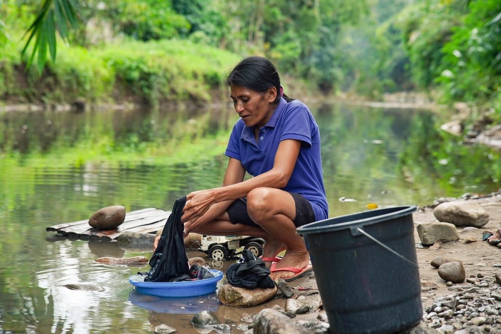 A woman sits, doing laundry by the riverbank