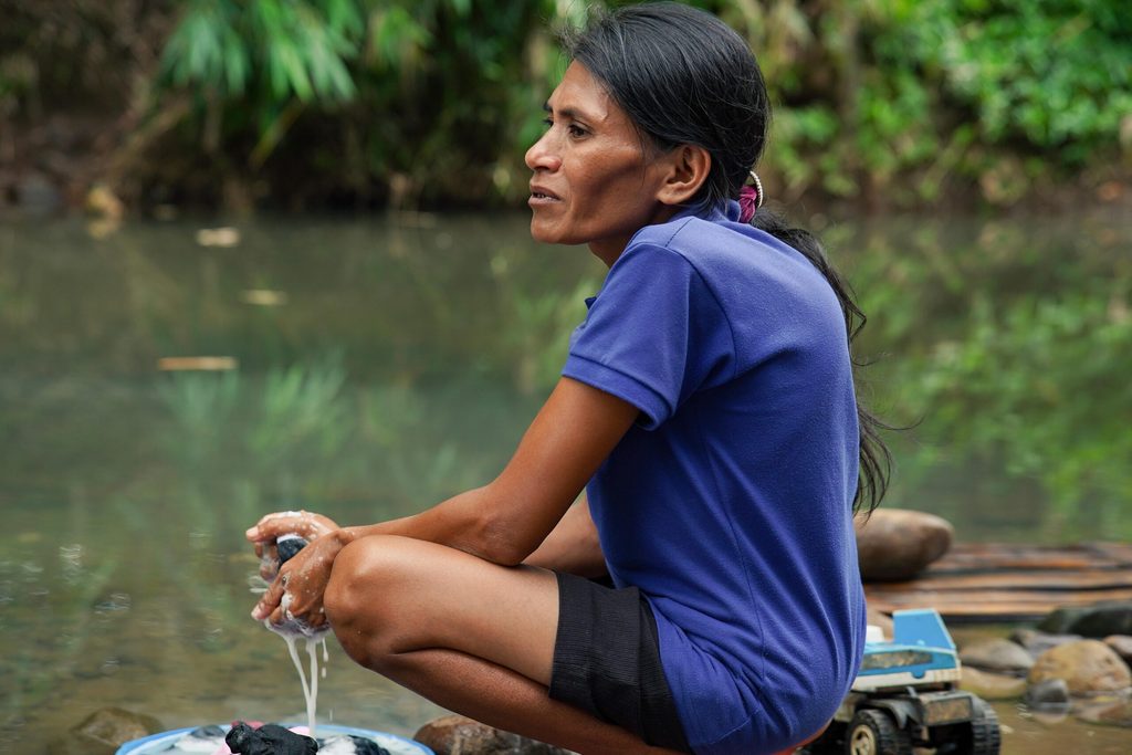 A woman sits doing laundry by the riverbank