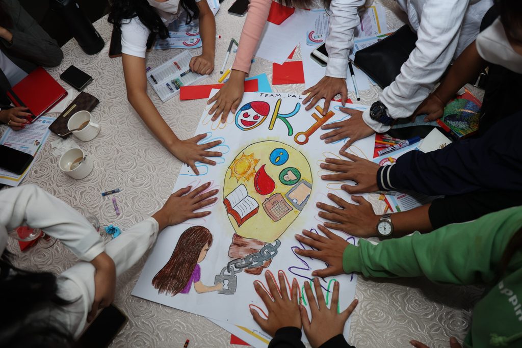 Multiple hands of young people press against a large paper to create a poster