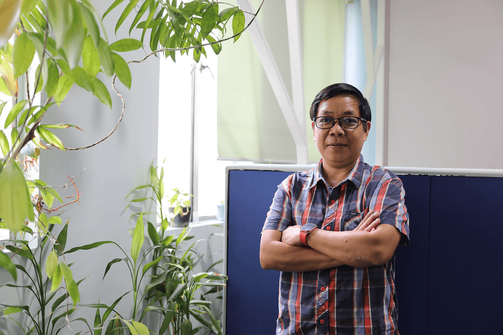 Woman wearing a plaid shirt poses for a photo by her work desk.