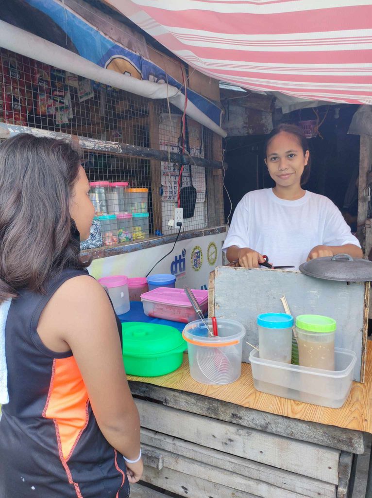 A young girl attends to her small store where a customer is lined up