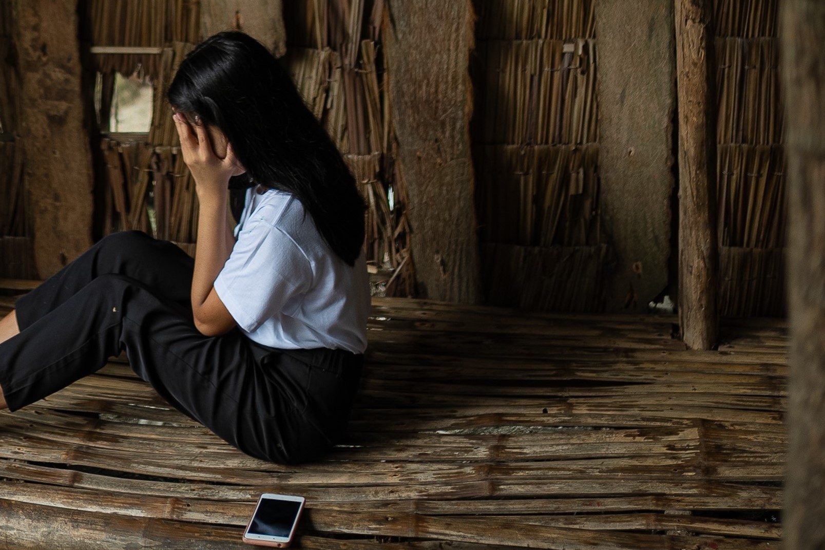 A young woman looks distressed as she sits beside her phone.