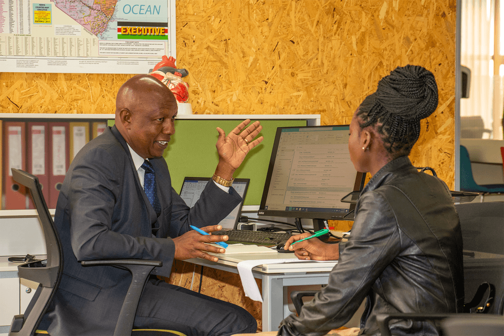 Linet and Sammy sitting opposite at a desk speaking. 