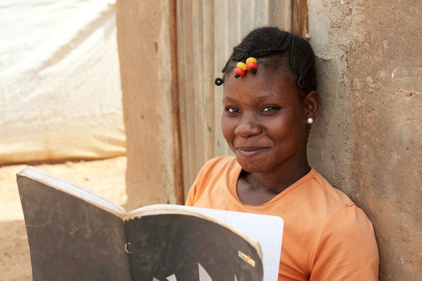 A girl reading a book and smiling at the camera